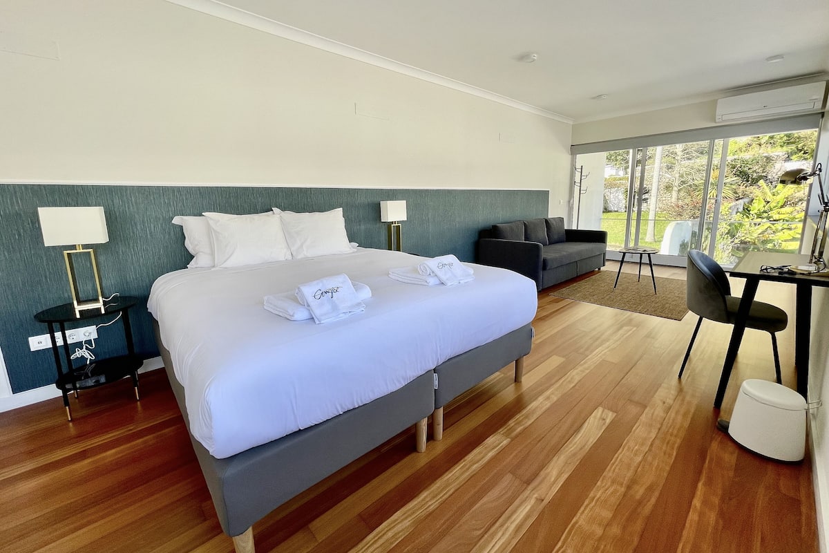 A hotel room with a large bed, a desk, a chair, and a sofa.