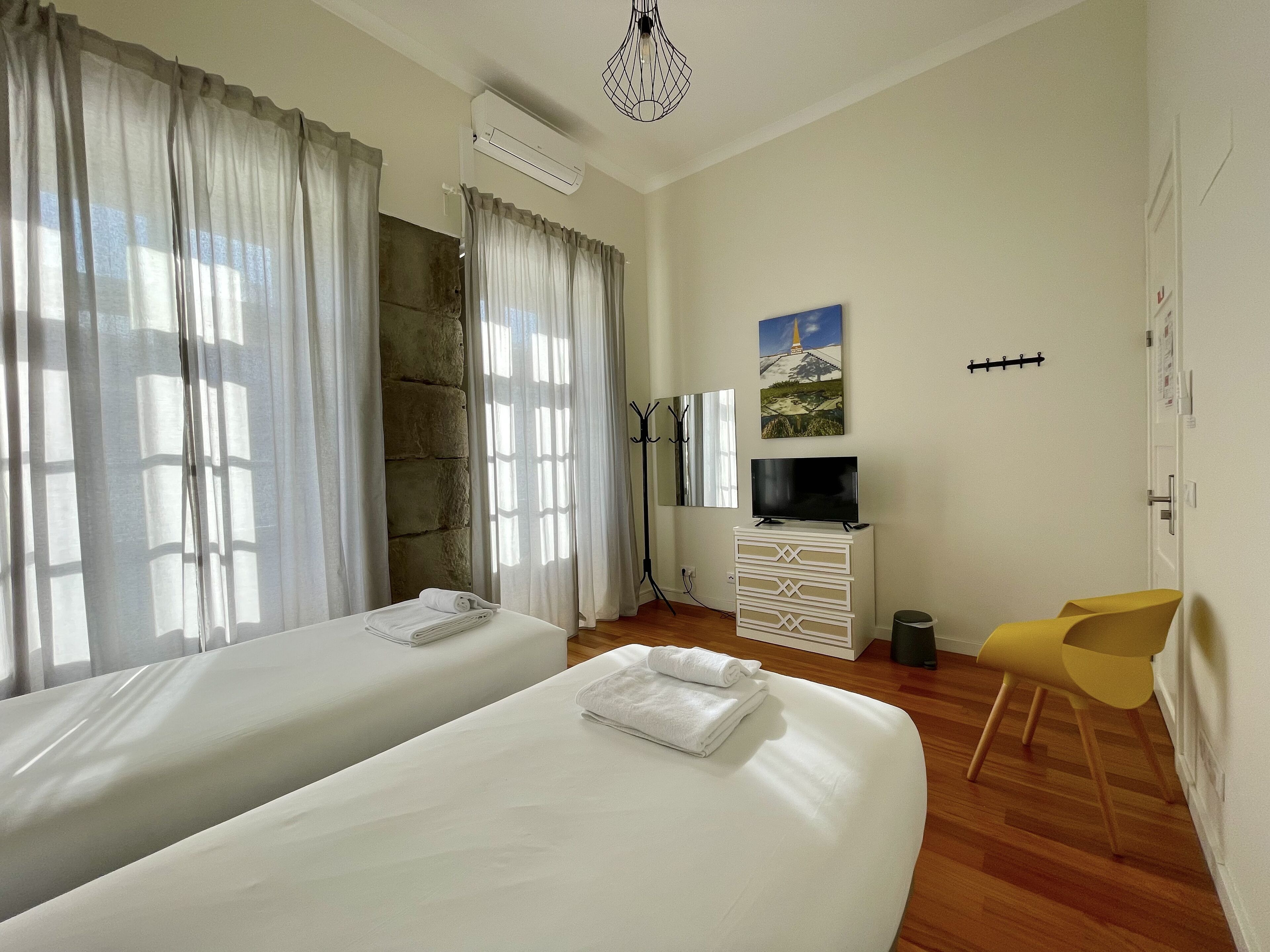 Habitación de hotel con dos camas, un televisor, perchero y una silla.