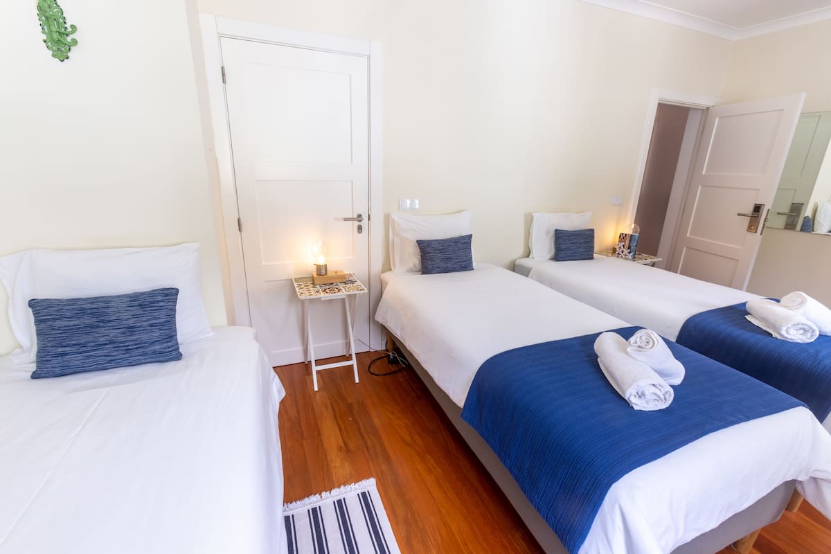 A hotel room with two single beds, a small table with a lamp, and a door leading to another room.