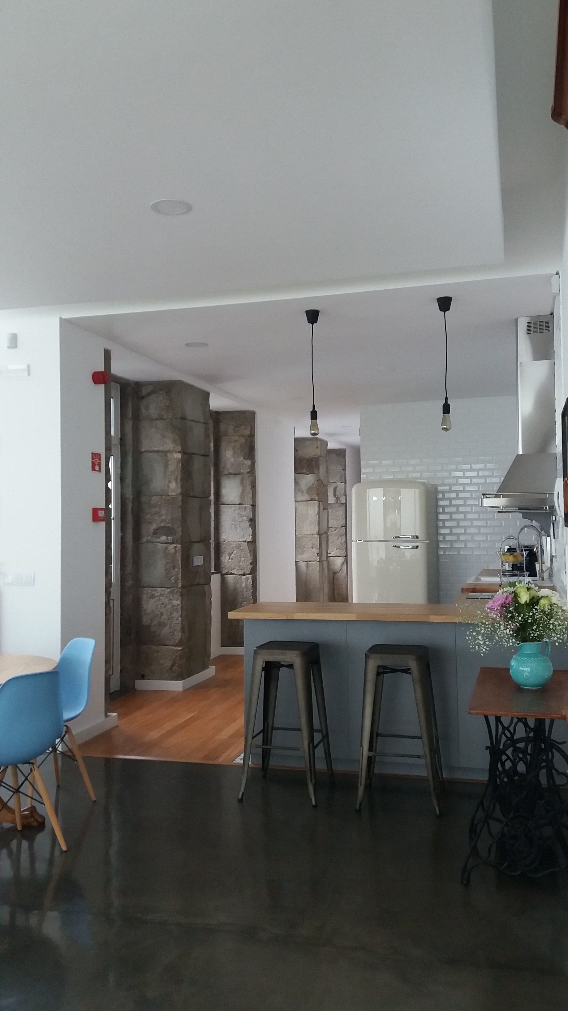A modern kitchen with a central island, bar stools, and a dining area with blue chairs.