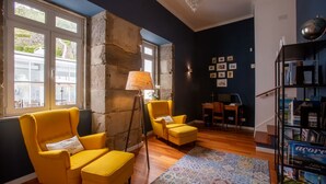 A room with a stone wall, yellow chairs, a patterned rug, and a bookshelf. - My Angra Charming House (Angra do Heroismo)