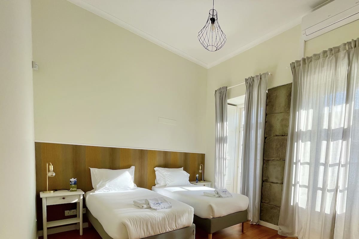 A hotel room with two beds, a wooden floor, a yellow chair, and a modern light fixture.