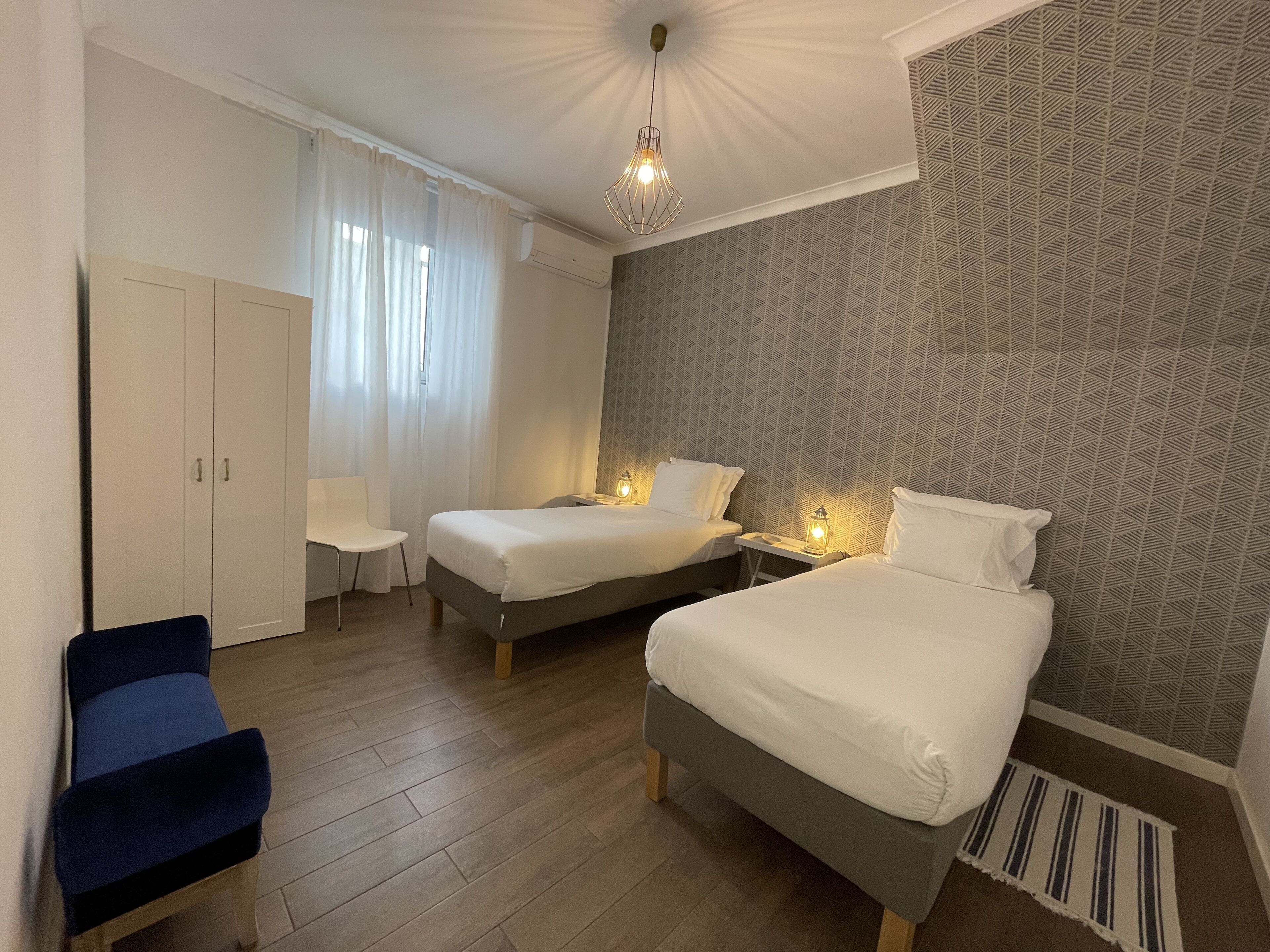 A hotel room with two beds, a desk, a chair, and a wardrobe.