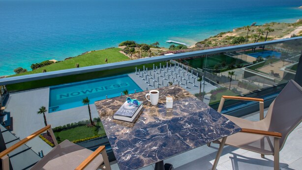 Un balcon avec vue sur la mer, une piscine et une table avec un livre, une tasse et une boîte.