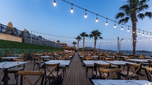 Un espace de restauration en plein air avec des tables et des chaises, des guirlandes lumineuses suspendues et des palmiers.