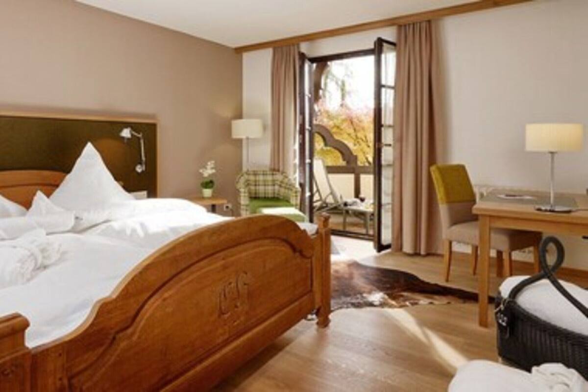 A hotel room with a wooden bed, a desk, a chair, and a view of the outdoors.