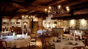 A rustic dining area with wooden beams, chandeliers, and stone walls. Tables are set with white tablecloths and chairs. - Hotel Eurener Hof (Trier)