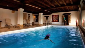 A swimming pool with a person swimming, lounge chairs, and a stone wall. - Hotel Eurener Hof (Trier)