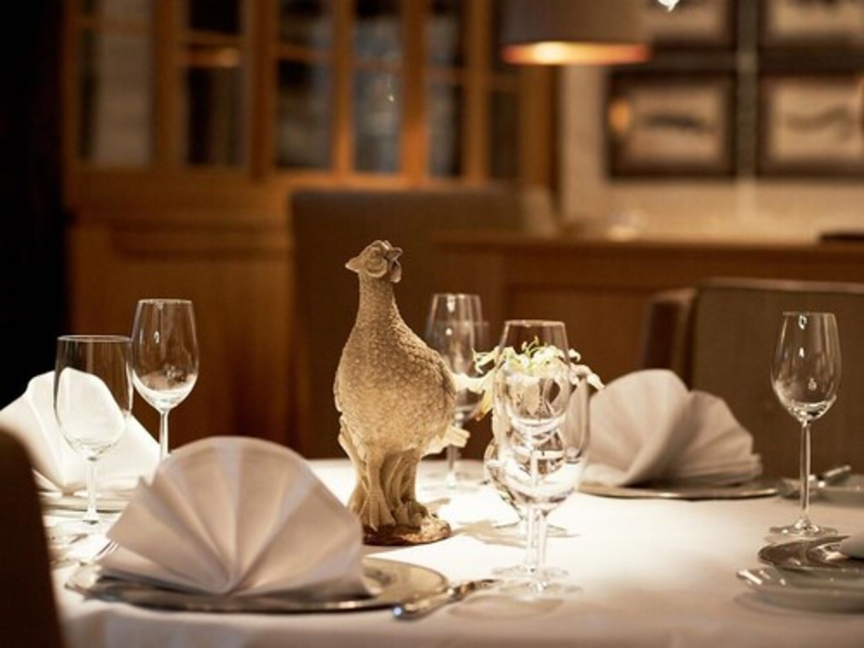 A dining table set with white tablecloths, wine glasses, and a decorative sheep figurine.