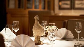 A dining table set with white tablecloths, wine glasses, and a decorative sheep figurine.