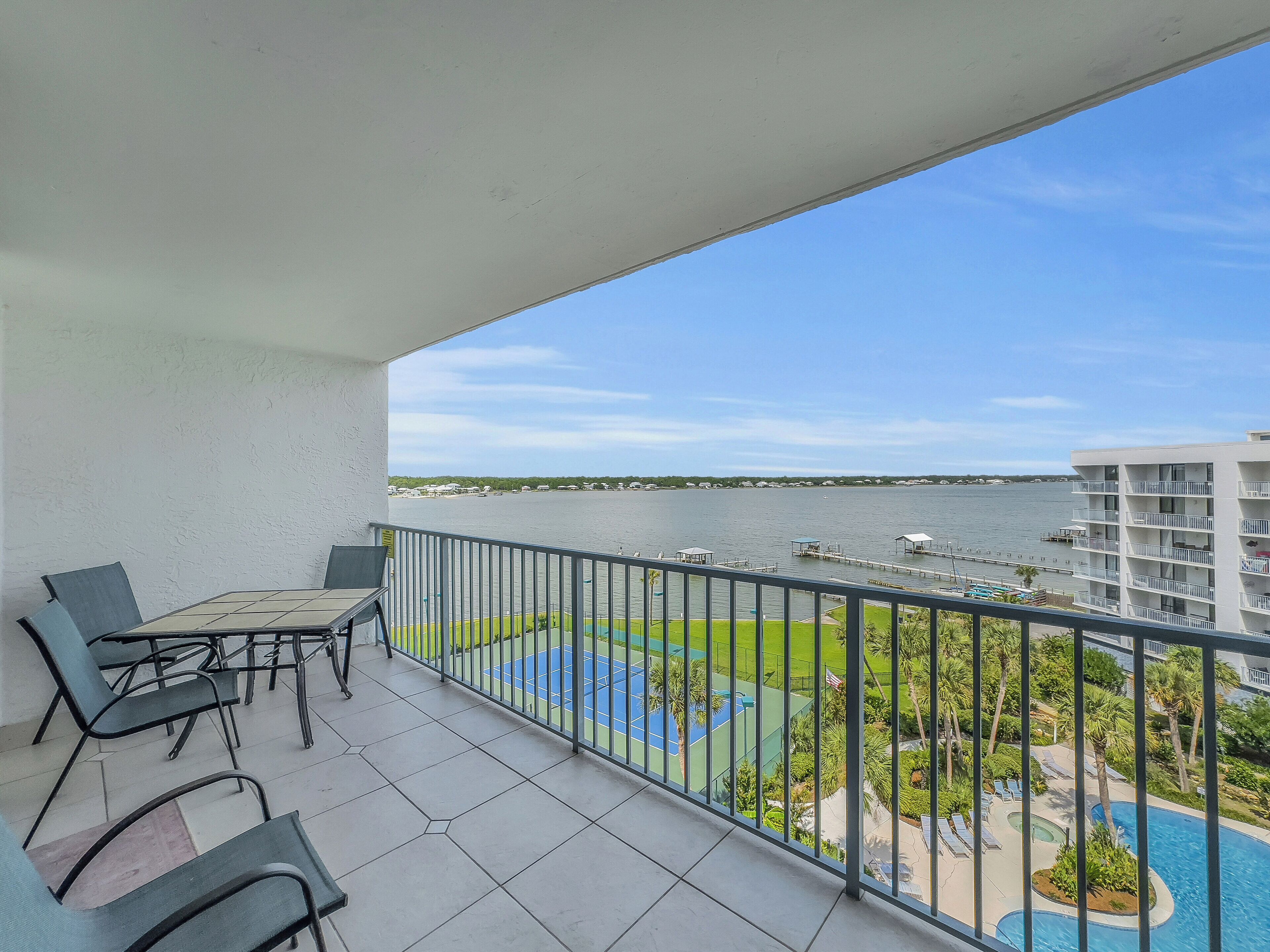 A balcony with a table and chairs, overlooking a swimming pool and a body of water.