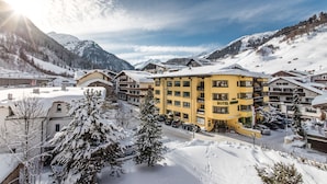 Een bergstad bedekt met sneeuw, met een opvallend geel hotel, omringd door besneeuwde bomen en bergen.