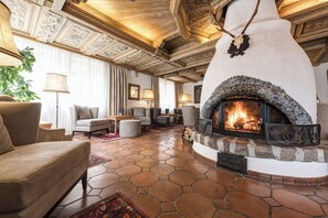 A cozy living room with a stone-tiled floor, a fireplace, and a high, intricately carved wooden ceiling. - Hotel Grieshof (Sankt Anton am Arlberg)