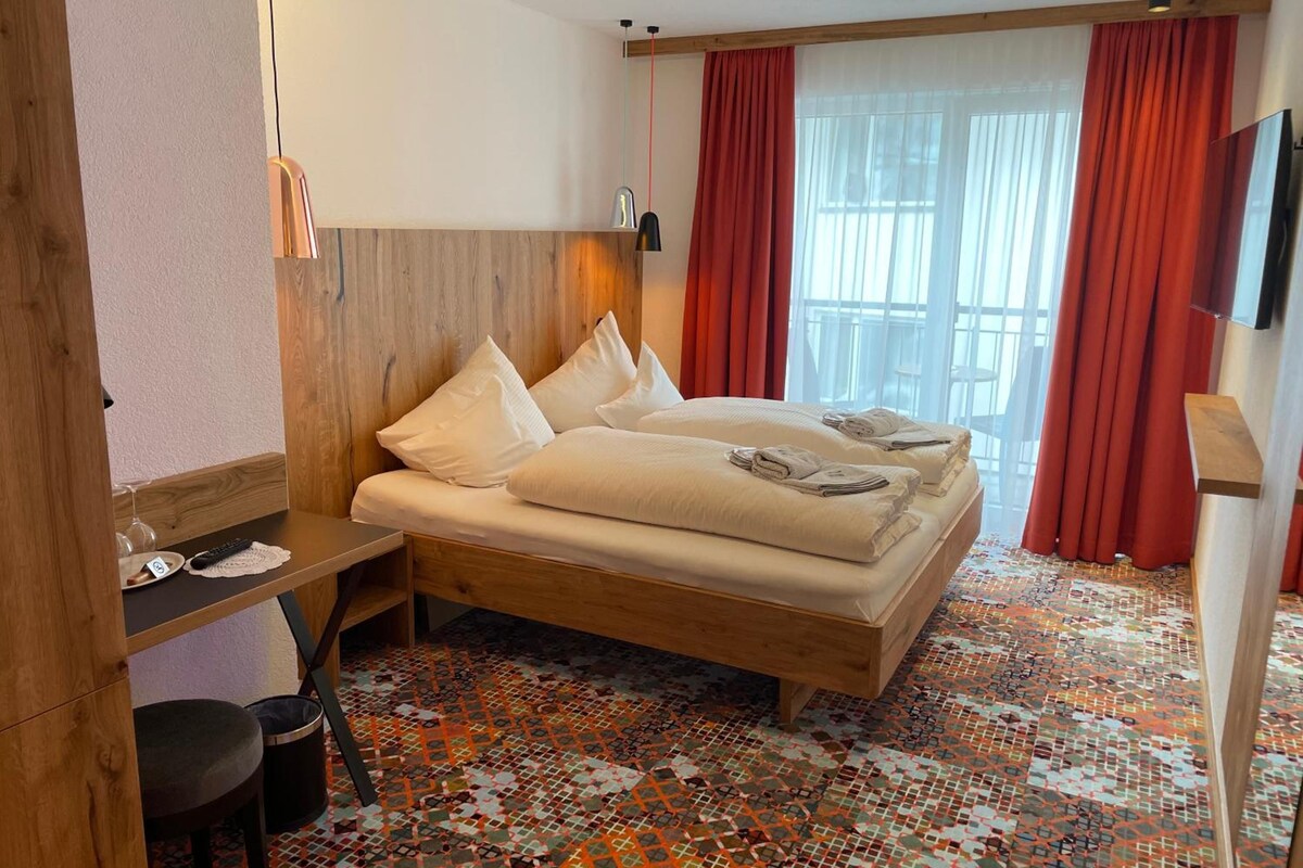 A hotel room with a bed, a desk, a chair, and a TV.