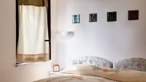 A bedroom with a bed, a nightstand, a wall-mounted lamp, and a window with curtains. - Relais Gea (Massa Lubrense)