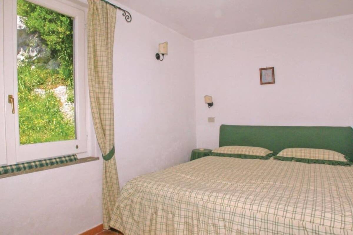 A bedroom with a bed, two wall-mounted lights, a window with curtains, and a small picture on the wall.