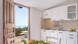 A kitchen with white cabinets, a sink, and a bowl of fruit on the table. - Relais Gea (Massa Lubrense)