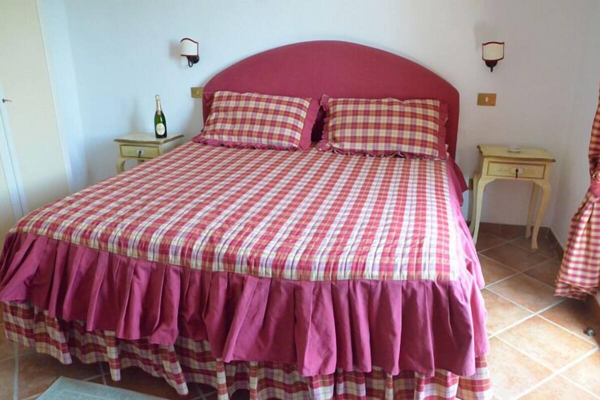 A bedroom with a large bed, two bedside tables, and a bottle of wine on one table.
