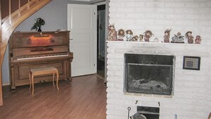 A room with a wooden piano, a fireplace with figurines, and a staircase. - 3 bedroom cozy home in Vimmerby (Vimmerby)