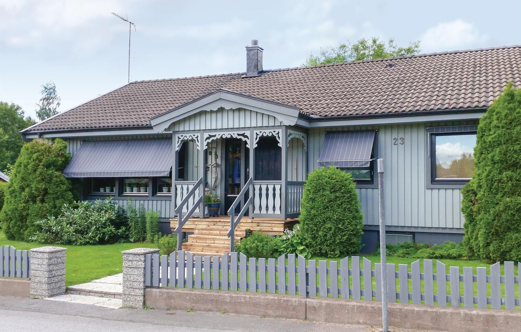 A two-story house with a grey facade, a tiled roof, and a front porch with a staircase.
