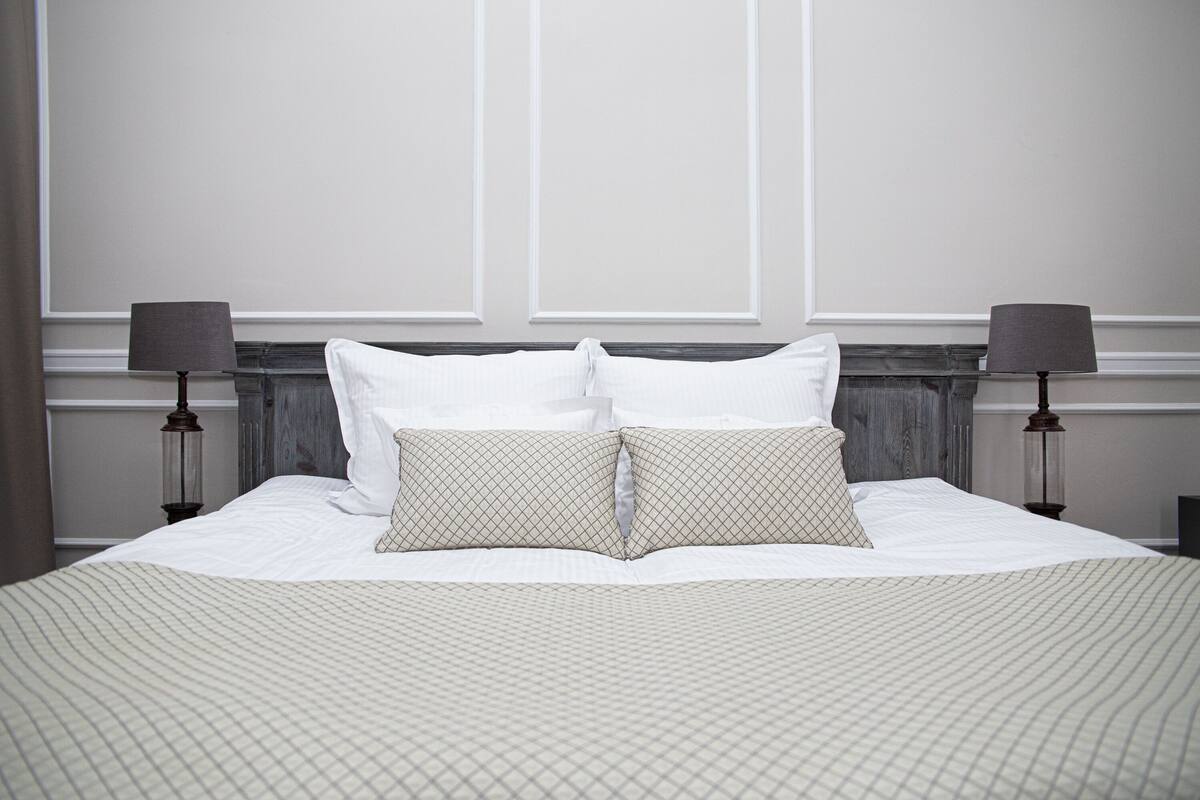 A neatly made bed with white linens and two pillows, flanked by two wall-mounted lamps.