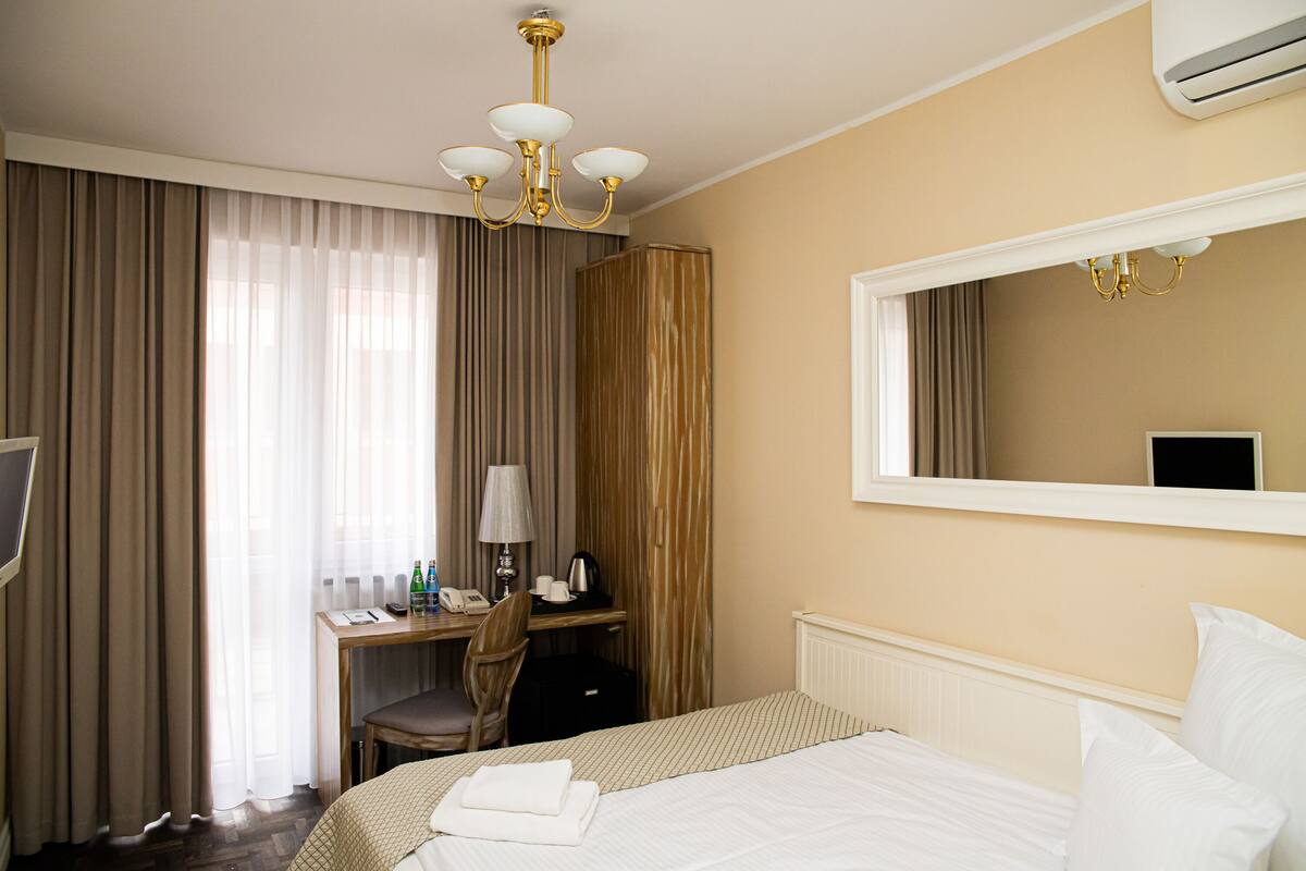 A hotel room with a bed, a desk with a chair, a lamp, a telephone, and a television.