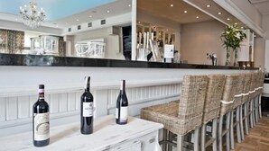 A bar area with three bottles of wine on a marble countertop, wicker chairs, and a mirrored wall reflecting the bar area. - Hotel Wodnik (Wroclaw)
