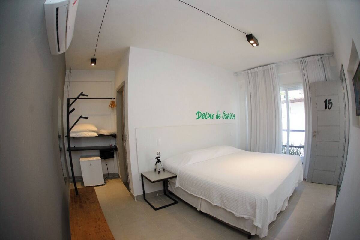 Une chambre avec un lit superposé, un bureau avec une lampe, une fenêtre avec des rideaux et une porte portant le numéro 15.