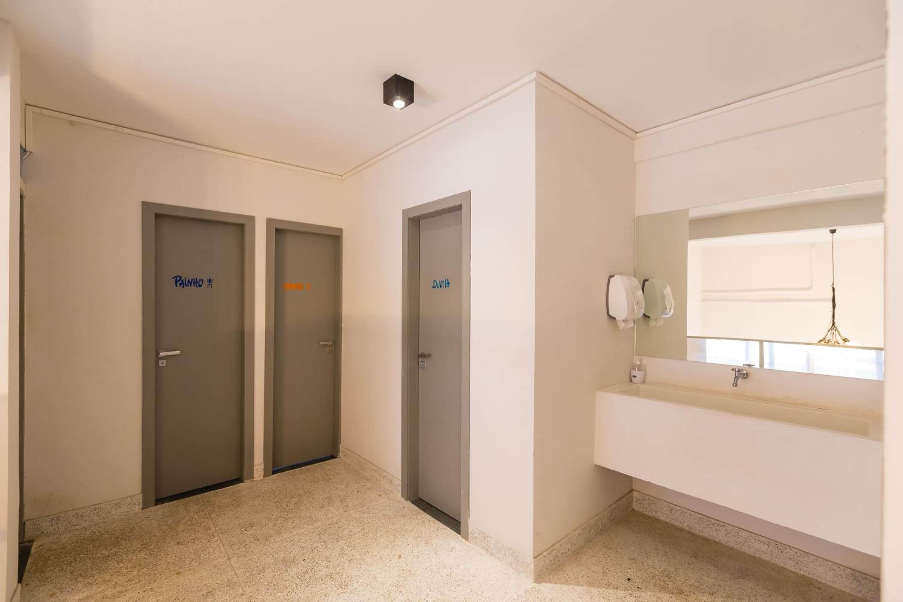 Un couloir avec trois portes portant l’inscription « Painho » et une salle de bain avec un lavabo et un miroir.