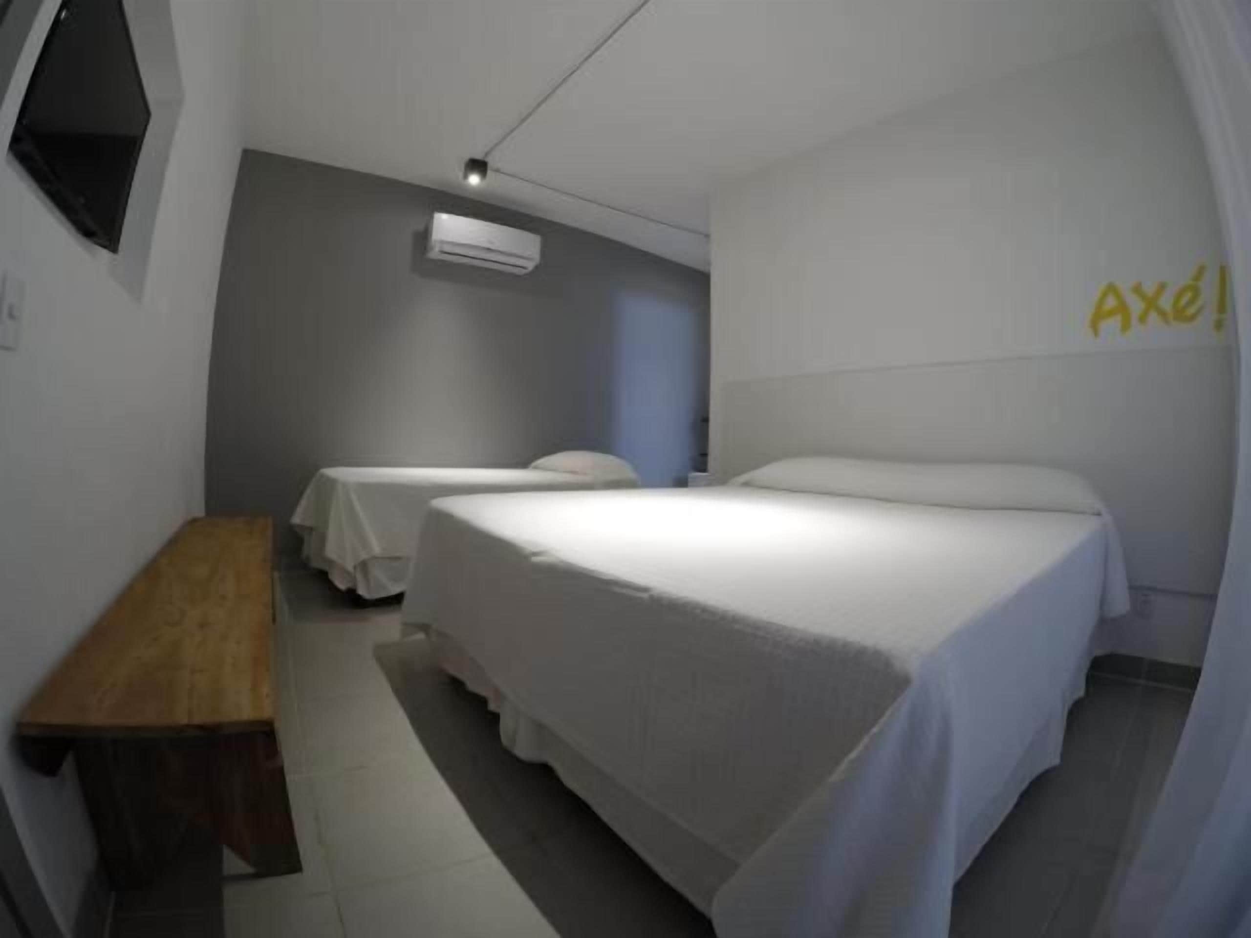 A hotel room with two single beds, a wooden bench, a wall-mounted air conditioner, and a curtain with the word "Axel" on the wall.