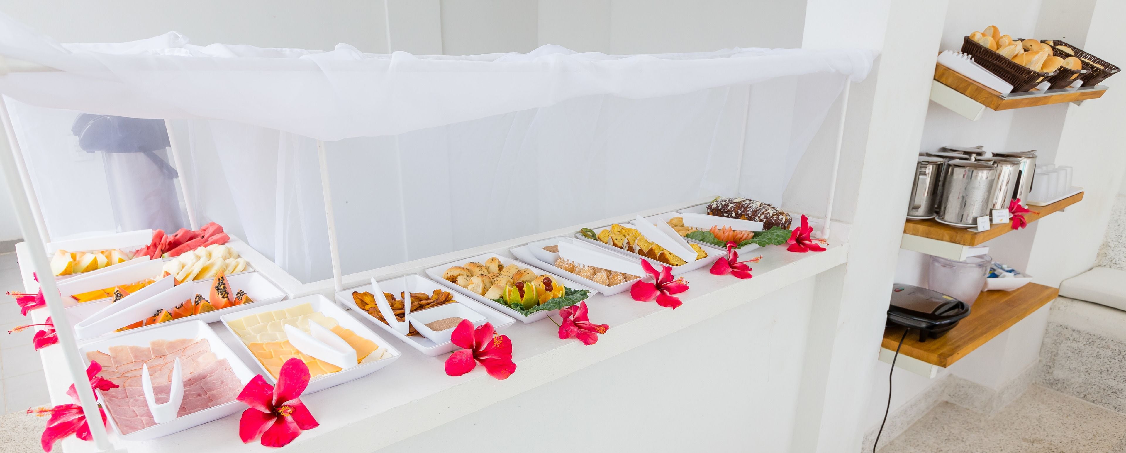 Disposição de buffet com diversos alimentos e flores tropicais.