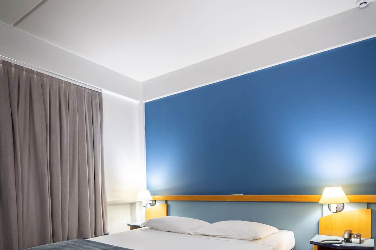 Hotellihuone, jossa on sänky, kaksi yöpöytää, lamppu ja verho.