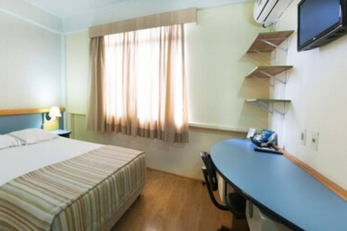 Hotellihuone, jossa on sänky, työpöytä, tuoli, televisio ja ikkuna, jossa on verhot.
