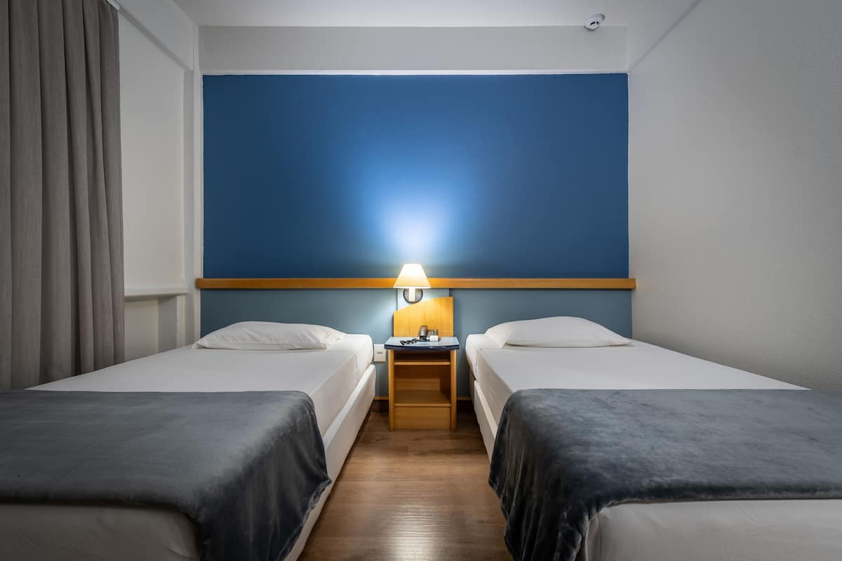 Hotellihuone, jossa on kaksi erillistä sänkyä, yöpöytä lampun kanssa ja suuri sininen seinä.