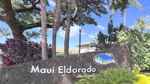 A sign for 'Maui Eldorado' with a logo, surrounded by tropical vegetation and a stone wall.