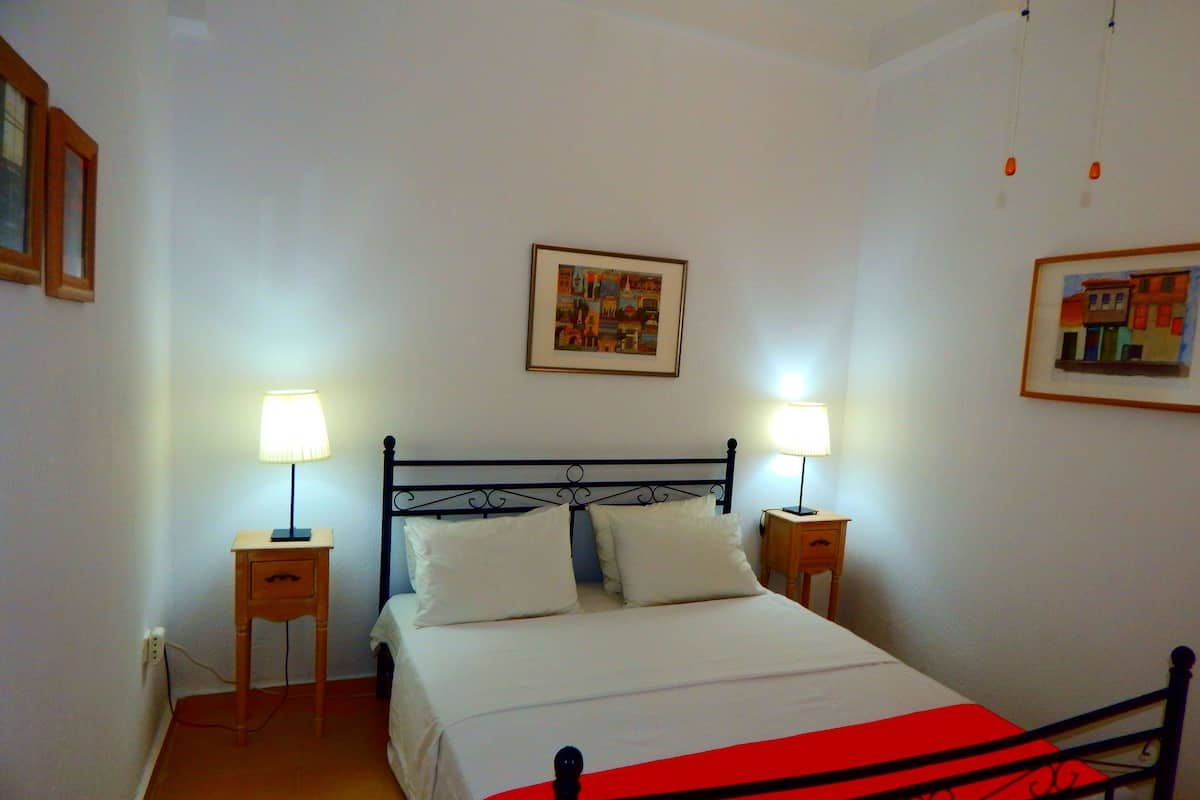 A bedroom with a bed, two bedside tables with lamps, and two framed pictures on the wall.