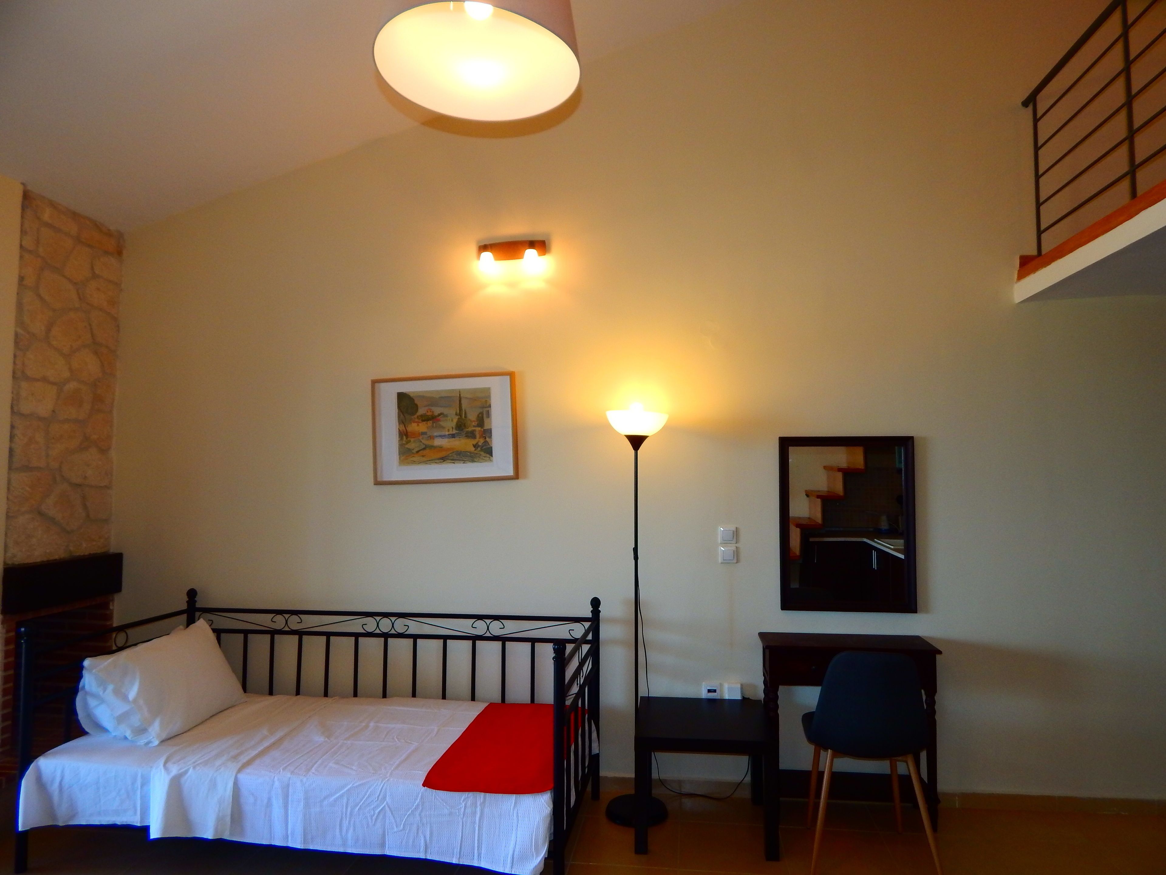 A bedroom with a bed, a desk, a chair, a lamp, a painting, and a staircase.