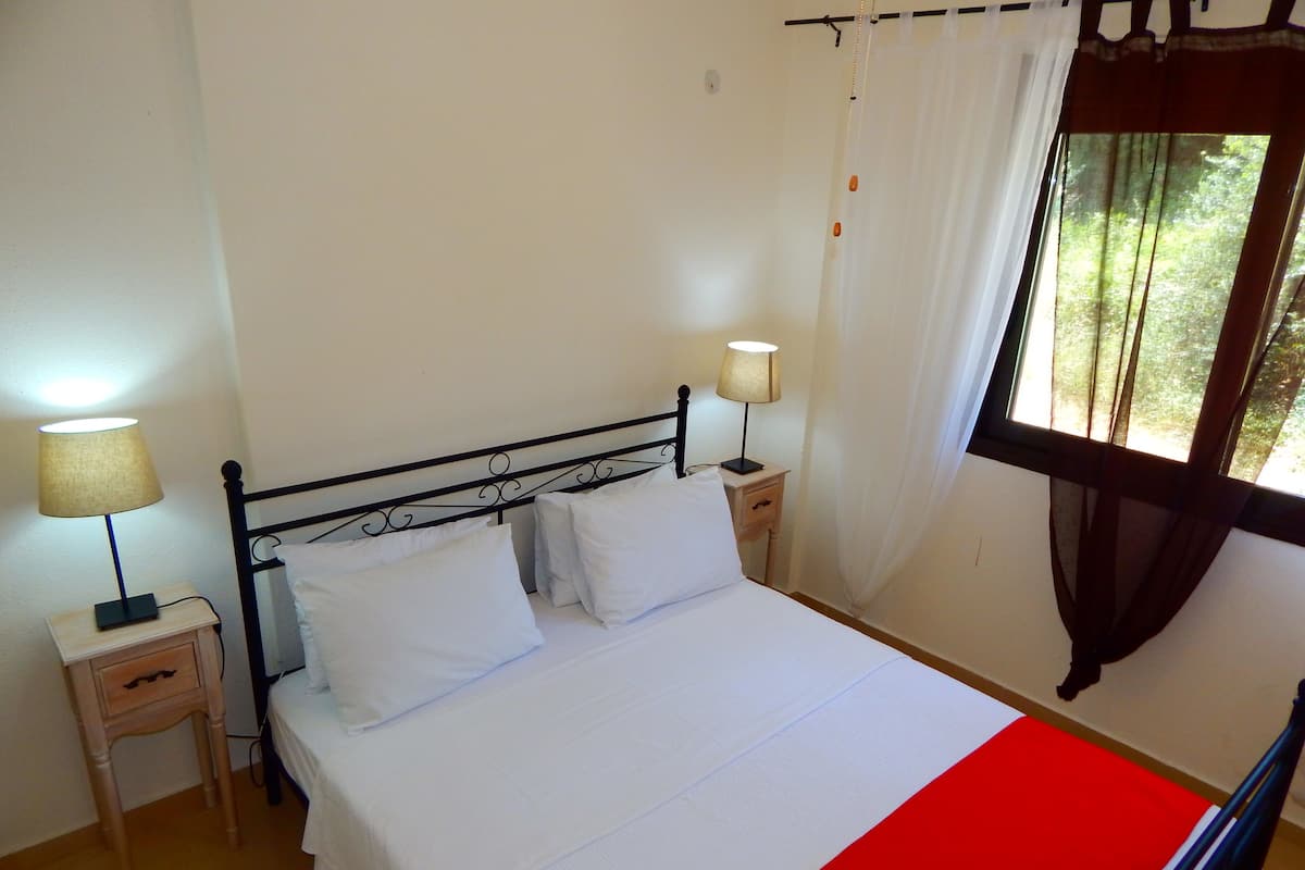 A neatly made bed with white linens, two bedside tables with lamps, and a window with curtains.