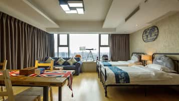 A hotel room with two beds, a sofa, a table with a Union Jack tablecloth, and a city view through large windows.