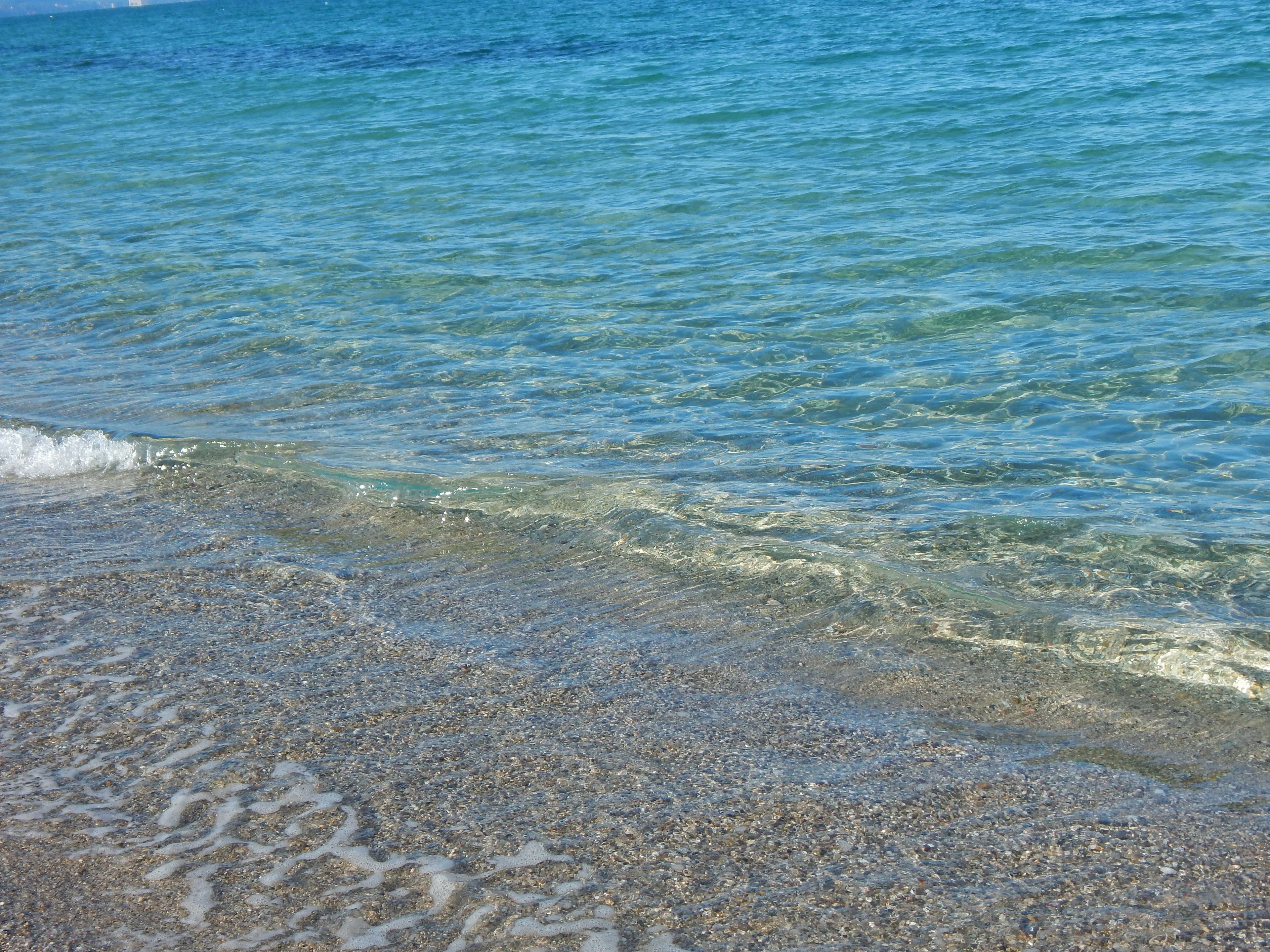 A clear view of a beach with shallow water and pebbles.
