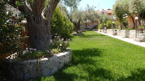A well-maintained garden with a stone wall, a large tree, and a clear pathway leading to a building with a red roof.