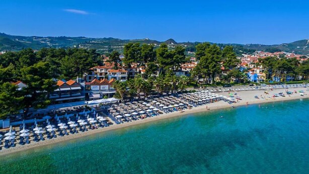 A coastal resort with beachside villas, clear blue waters, and a sandy beach with umbrellas.
