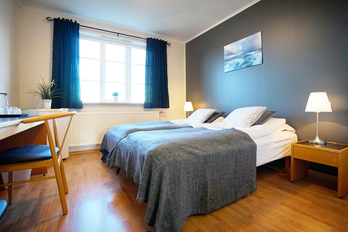 Un dormitorio con dos camas, un escritorio, una silla, una lámpara y una ventana con cortinas.