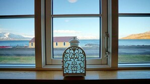 A view through a window with a decorative lantern in the foreground, a building across the water, and a clear sky. - Grenivík Guesthouse (Grenivík)