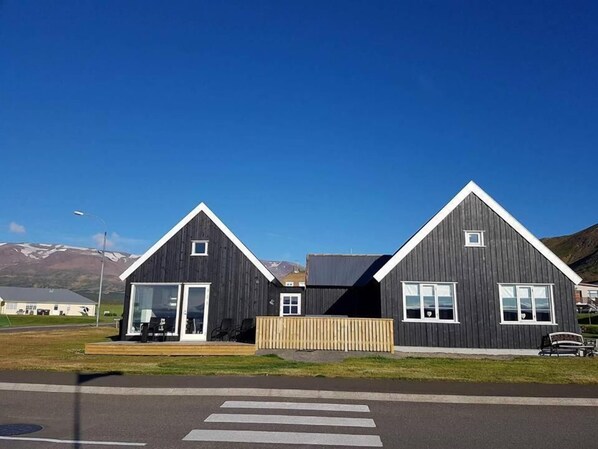 Dois edifícios modernos com fachada escura e detalhes em branco, apresentando grandes janelas e um deck de madeira na frente.