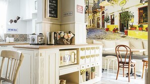 Una cocina con un armario blanco, un tostador y una cafetera. Hay una zona de comedor con una mesa y sillas blancas.
