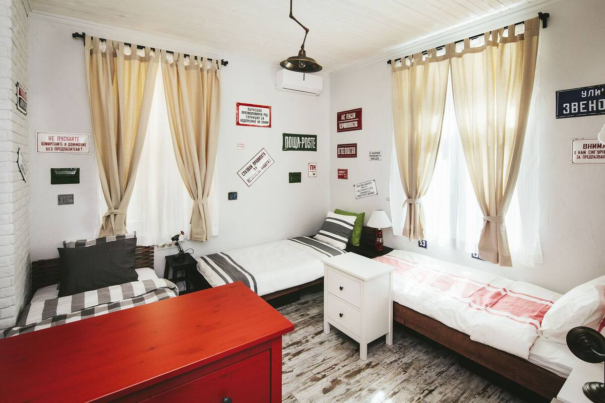 A bedroom with two beds, a red dresser, a white nightstand, and a wooden floor.