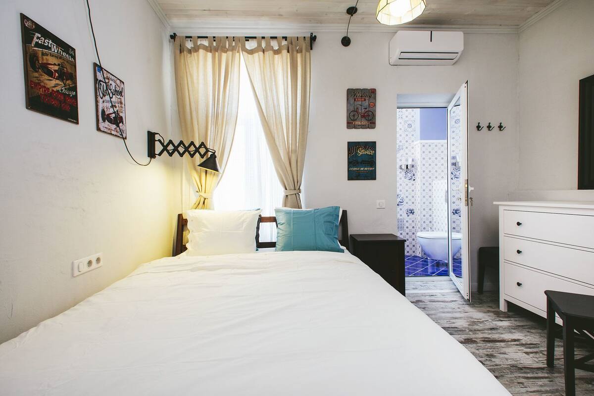 A bedroom with a bed, a nightstand, a dresser, and a bathroom visible through an open door.