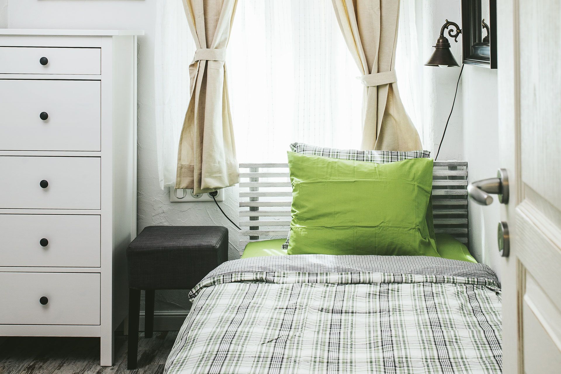 Quarto com cama, cômoda, mesa de cabeceira e janela com cortinas.