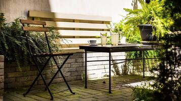 A patio with a wooden bench, a table, and potted plants.